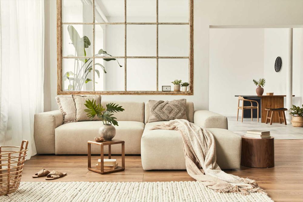 Bej tonlarında modern bir oturma odası. Büyük pencere, bitkiler ve minimalist mobilyalarla ferah bir atmosfer yaratılmıştır.